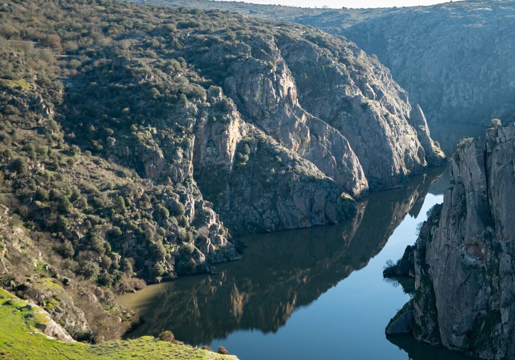 The Douro river running between steep rocky cliffs near Miranda do Douro, with green slopes in the foreground.