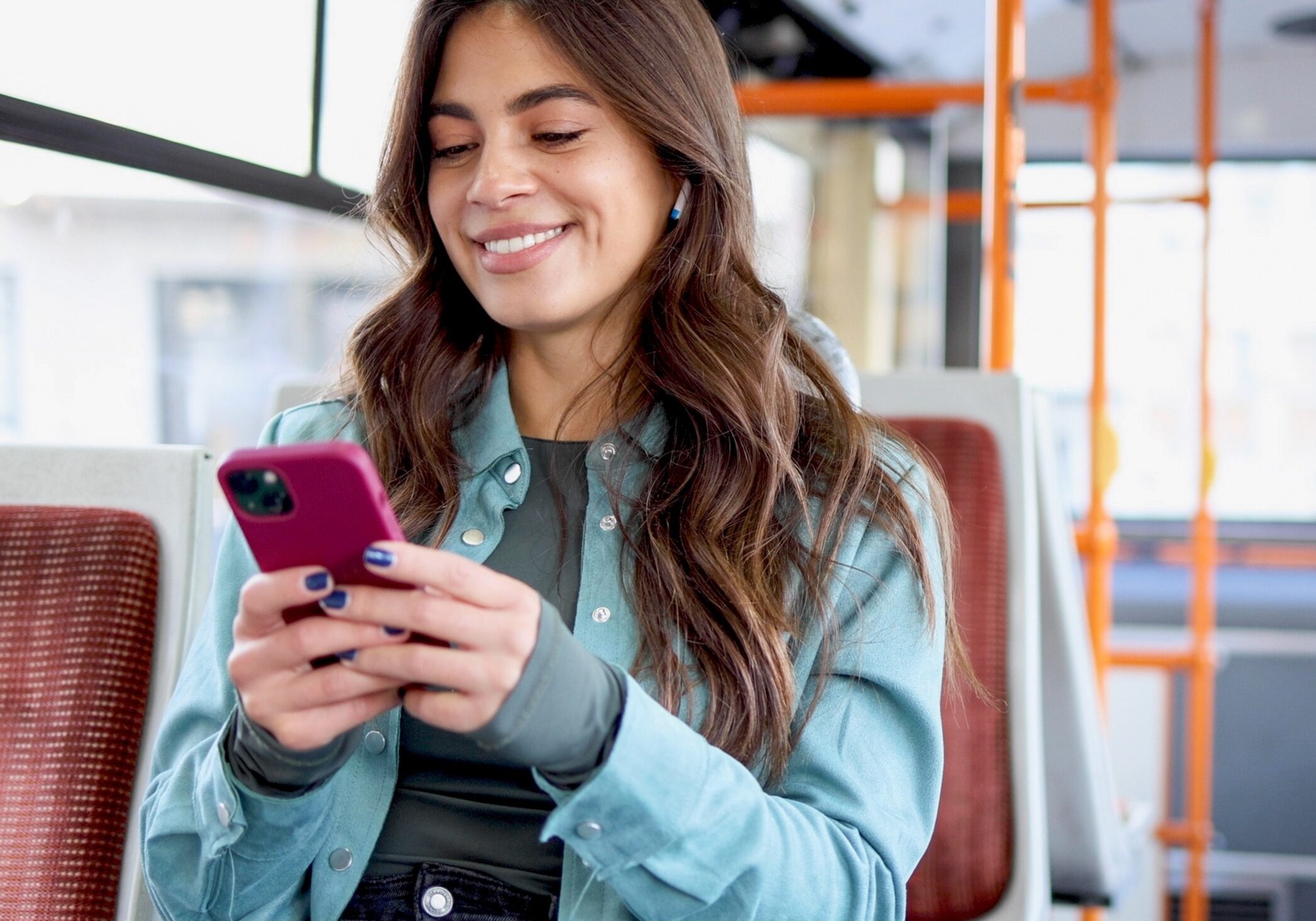 young woman on a bus, looking at her phone, smiling