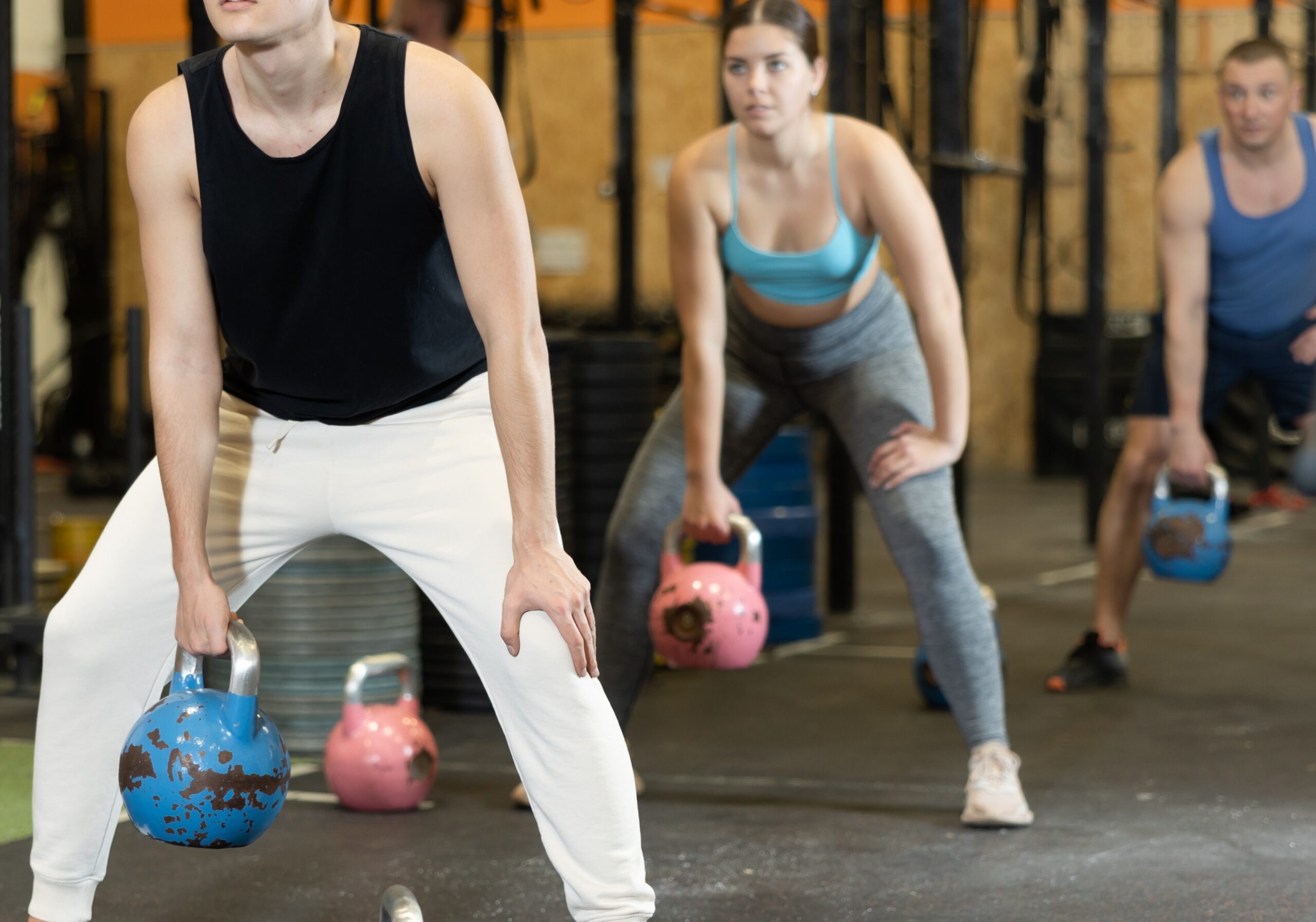 three people in the gym lifting kettlebells