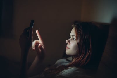 woman staring at cell phone in dark room, scrolling