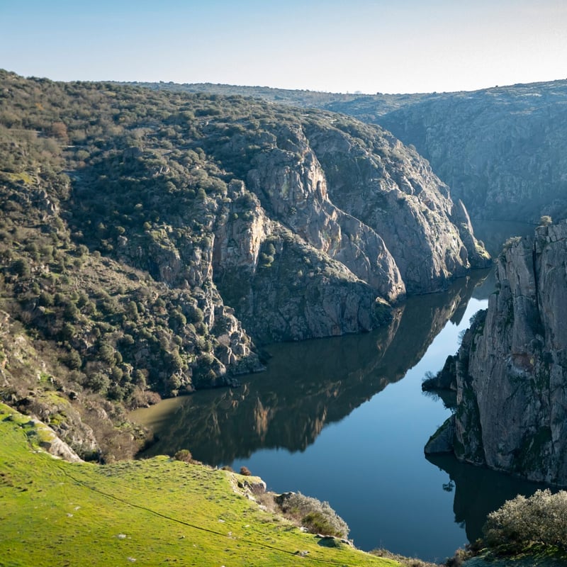 The Douro river running between steep rocky cliffs near Miranda do Douro, with green slopes in the foreground.